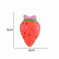 Jouet à presser fraise avec yeux exorbités et nœud rose, dimensions 9 cm x 6 cm - Fraise Rouge
