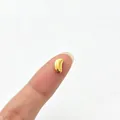 Macro detail of a tiny gold bean-shaped stainless steel spacer bead on a finger for scale - Acacia Bean Style (6284455362261)
