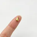 Detailed macro view of a tiny gold drop-shaped stainless steel spacer bead on a fingertip - Water Drop Style (6284455362262)