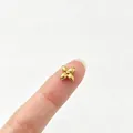 Primer plano de una pequeña cuenta de acero inoxidable con flor de cuatro pétalos en un dedo. - Gran Trébol de Cuatro Hojas / Dorado