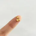 Detalle de un pequeño colgante de cereza dorada sobre la yema del dedo para tamaño. - Cereza (P4-5)