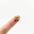 Detailansicht eines kleinen vergoldeten Kirschenanhängers in Herzform auf einer Fingerspitze - Kirsche mit Strass Stil (4#)