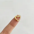 Makroaufnahme eines goldenen Herzanhängers mit Zirkonia auf einer Fingerspitze - Einzelner Anhänger (Ohne Kette) / Goldenes Herz (Klarer Strass)