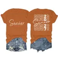 Vista fronte e retro della t-shirt grafica arancione Senior Class of 2027 da donna girocollo - Taglia S / Top / arancio bruciato (scritta bianca)