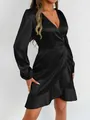 Close-up detail of a black satin long-sleeve wrap dress with ruffled hem on a model. - XS / Top And Bottom / Black