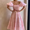 Dettaglio di un abito rosa con spalle scoperte, maniche a sbuffo e gonna a balze. - Rosa