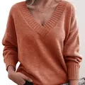 Close-up detail of a women's loose V-neck knitted sweater in elegant burnt orange - Orange