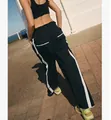 Rear view of black Y2K straight-leg sports pants with white side stripes in outdoor setting - S / Bottoms / Black