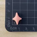 Macro view of a mini pink four-pointed star resin accessory on a black grid mat - Orange