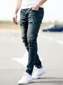 Detailed close-up view of men's slim-fit blue denim jeans featuring distressed knee accents. - Vintage Blue