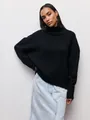 Μοντέλο που φοράει μαύρο oversized πλεκτό πουλόβερ με ζιβάγκο και ανοιχτόχρωμη τζιν φούστα - S / Tops / Μαύρο