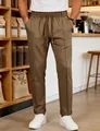 Detail of men's brown drawstring casual trousers with elegant front crease in cafe setting - Camel
