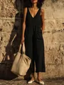 Model in black V-neck cotton linen jumpsuit with wide-leg cropped pants and a woven straw bag - S / Top And Bottom / Black