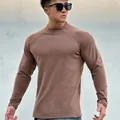 Man in a brown slim fit muscular long sleeve crew neck fleece base layer shirt against a wall - Camel Gray