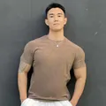 Close-up view of a muscular man wearing a brown athletic crew neck t-shirt outdoors. - M / Tops / Crew Neck / Camel Gray