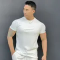 Muscular model wearing a white athletic fit short-sleeve T-shirt against a dark wall - M / Tops / Crew Neck / White