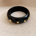 Vintage schwarzer Armreif mit goldenen Stern- und Punktnieten auf beigem Stoffhintergrund - Schwarz Polierte Sternnieten / Schwarz-Gold