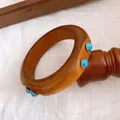 Nahaufnahme eines hölzernen Retro-Armreifs mit eingelegten blauen Türkissteinen - Massivholz Türkis Einlegestil / Bräunen-Türkis