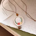 Detailed view of a handmade crochet hat pendant necklace with an acorn charm and flowers. - White Straw Hat / White (Coffee Cord)