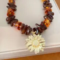 Primo piano di una collana di perle in resina con un grande ciondolo a forma di girasole d'oro - Girocollo Girasole / Caffè