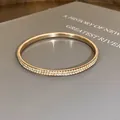 Detail van een roségouden armband met dubbele rij kristallen op een boekdecoratie - Goud (Geel)