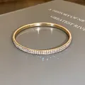 Close-up van een goudkleurige armband met dubbele rij strass-steentjes op grijs - Goud (AB Kleur)
