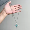 Gros plan d'un collier avec pendentif croix en zircon vert menthe tenu dans la main - Collier Pendentif Croix / Argent-Vert