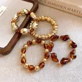 Primer plano detallado de pulseras elásticas geométricas en tonos ámbar y dorado - Pulsera - Dorado / Café