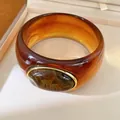 Detail view of a chunky amber resin bangle with an oval marbled stone in gold-tone setting - Geometric Open Style (43#)
