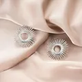 Elegant silver sunburst stainless steel stud earrings displayed on pink silk fabric background - Hollow Sun Flower Silver Style (E1341-B) / 1 Pair Pack / Steel