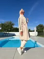 Scatto lifestyle di un cappotto teddy crema con strisce nere accanto a una piscina blu. - Taglia S / Top / Bianco avorio