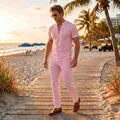 Male model wearing a pink lace-up short-sleeve top and trousers set on a beach at sunset - Pink