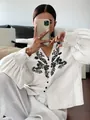 Detailed macro view of white long sleeve blouse featuring elegant black floral embroidery - S / Tops / White