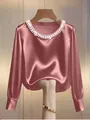 Close-up detail of an elegant mauve pink satin blouse featuring a pearl-embellished round neckline. - Pink
