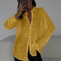 Close-up view of the glittering yellow sequin texture on a long-sleeved button-up blouse - Gold