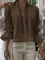 Detalle de blusa plisada marrón con elegantes puños de volantes y un corte holgado. - Marrón