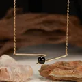 Detailed macro view of a geometric gold bar pendant necklace with a black onyx bead - Natural Black Agate / Gold
