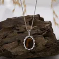 Close-up of a tiger eye gemstone pendant on a silver box chain against a natural wood bark. - Natural Tiger Eye Necklace / Silver