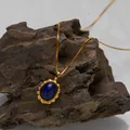 Close-up detail of a vintage gold necklace with an oval lapis lazuli stone pendant on a rock - Natural Lapis Lazuli Necklace / Gold