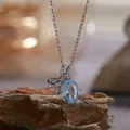Close-up van S925 zilveren ketting met blauwe edelsteen strikhanger op een rotsblok. - Strik Ketting (R393) / 40+5cm Kettinglengte / Lichtblauw (Natuurlijke Topaas)