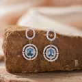 Nahaufnahme der S925-Silberohrringe mit ovalem blauem Topas und glitzernden Zirkonen. - Natürlicher Topas Ohrstecker / Silber