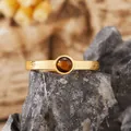 Primo piano di un anello dorato testurizzato con una pietra occhio di tigre tonda. - occhio di tigre naturale / Oro