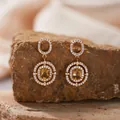 Nahaufnahme von vergoldeten Ohrringen mit gelben Edelsteinen auf einem rauen Stein - Natürlicher Citrin Ohrstecker / Gold