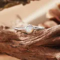 Detailed close-up of a sterling silver ring with a round opal gemstone on natural wood - Open Ring / Natural Opal