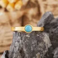 Dettaglio di un anello in argento placcato oro con pietra turchese tonda e finitura materica - Turchese naturale / Oro