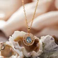 Detailaufnahme einer vergoldeten S925-Silberkette mit blauem Edelsteinanhänger auf einer Muschel. - Natürlicher Topas Halskette / Gold