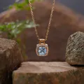 Primer plano de un collar con colgante de topacio azul cuadrado con halo sobre rocas. - Topacio (N399) / Dorado