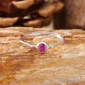 Dettaglio di un anello d'argento con ametista su sfondo di pietra naturale grezza. - Rubino