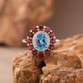 Detailaufnahme eines Silberrings mit blauem Topas und einem Kranz aus roten Granaten. - Ring / Natürlicher Topas / Blau