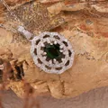 Detailed macro view of a dark green gemstone pendant with floral silver halo on natural rock. - Natural Diopside Necklace